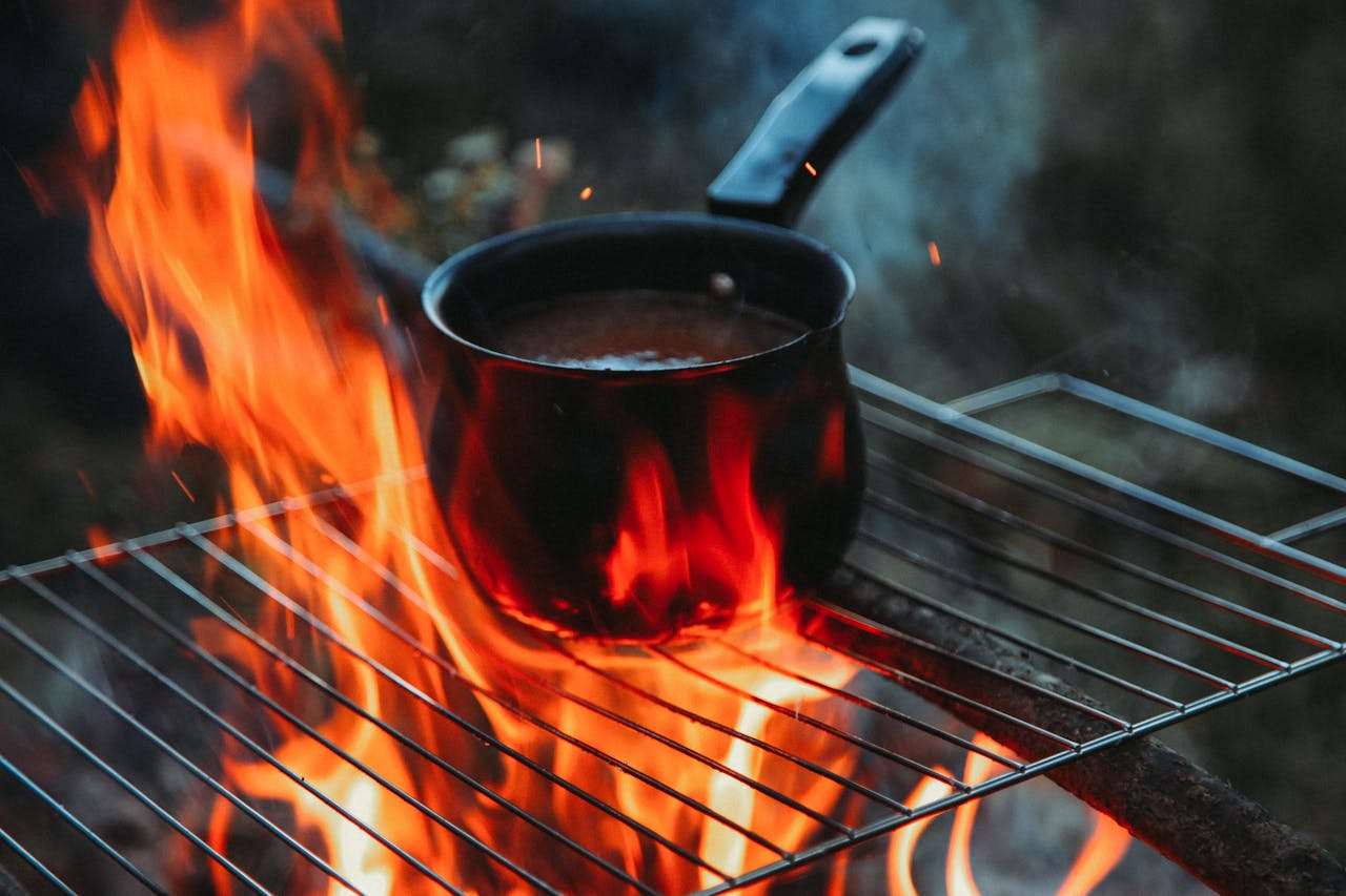 A black pot cooking over a blazing campfire on a metal grill. Perfect for outdoor cooking themes.